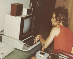 A man sitting in a wheelchair using a computer with a navigation stick.